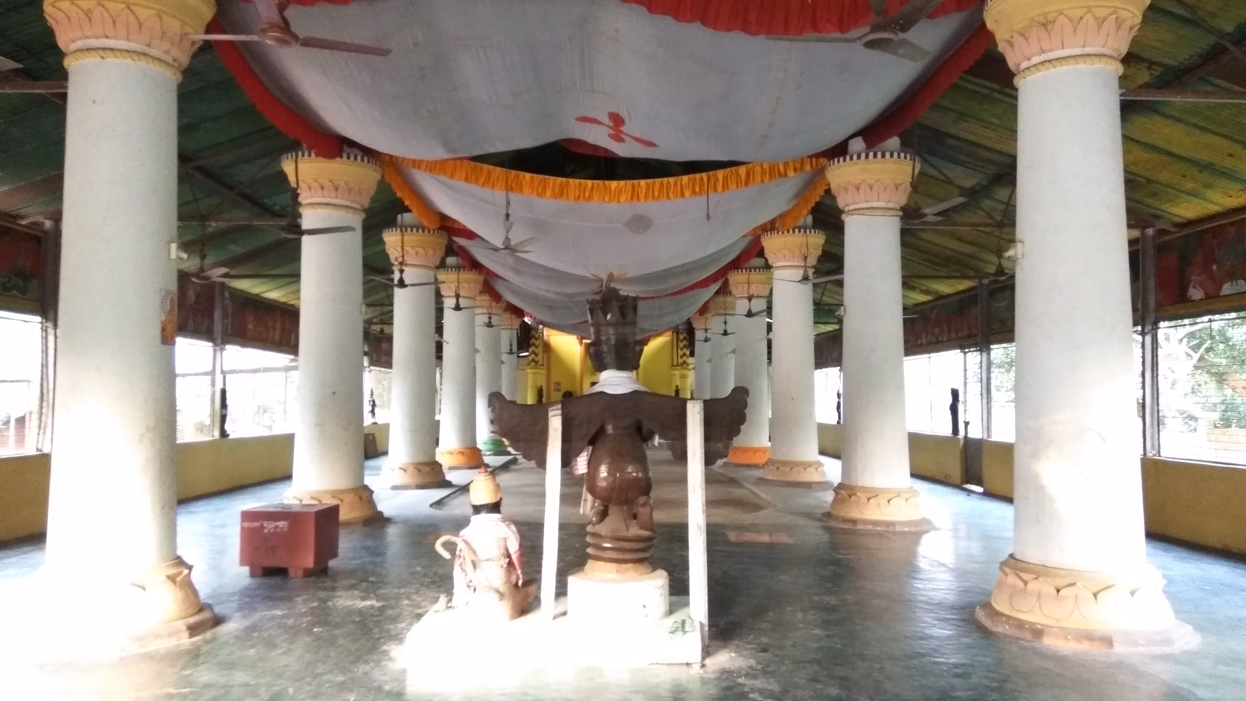 Rows of lotus-capital pillars under a fabric canopy lead to the central shrine inside the Garamur Sattra namghar on Majuli