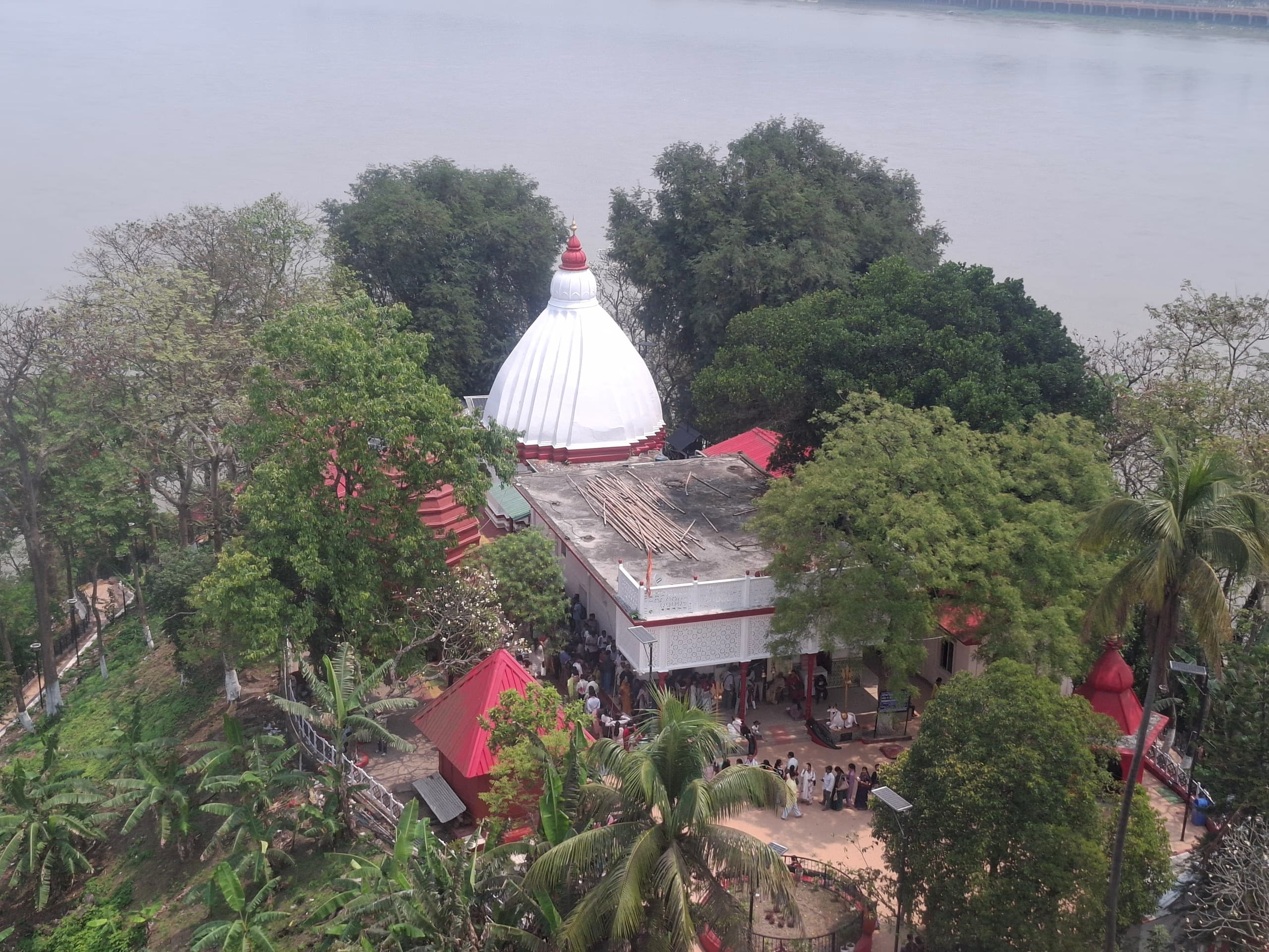 Aerial view of the white-domed Umananda Siva temple and its red-roofed shrines on the wooded Peacock Island, the Brahmaputra surrounding it
