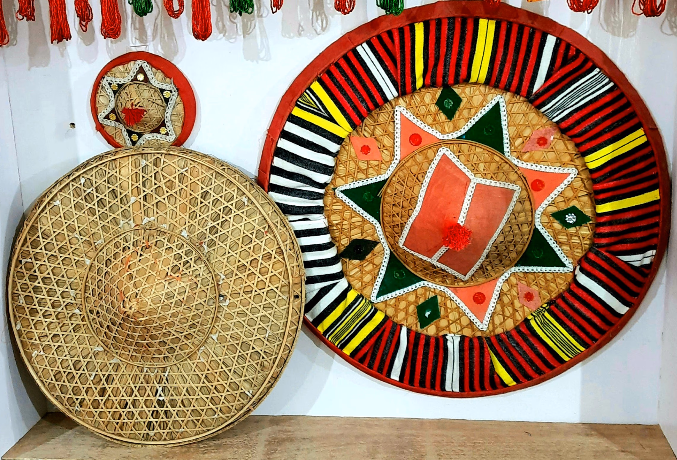 An undecorated bamboo japi beside two japis covered in red, green and white cloth with star appliqué