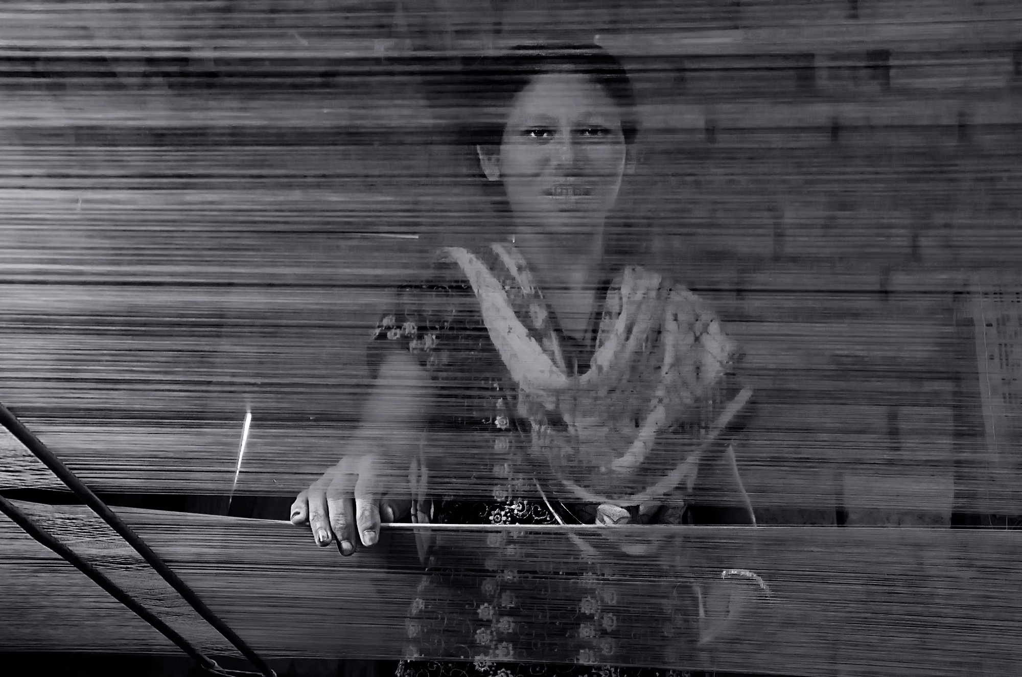 A woman weaver seen through the stretched warp threads of a handloom at Sualkuchi