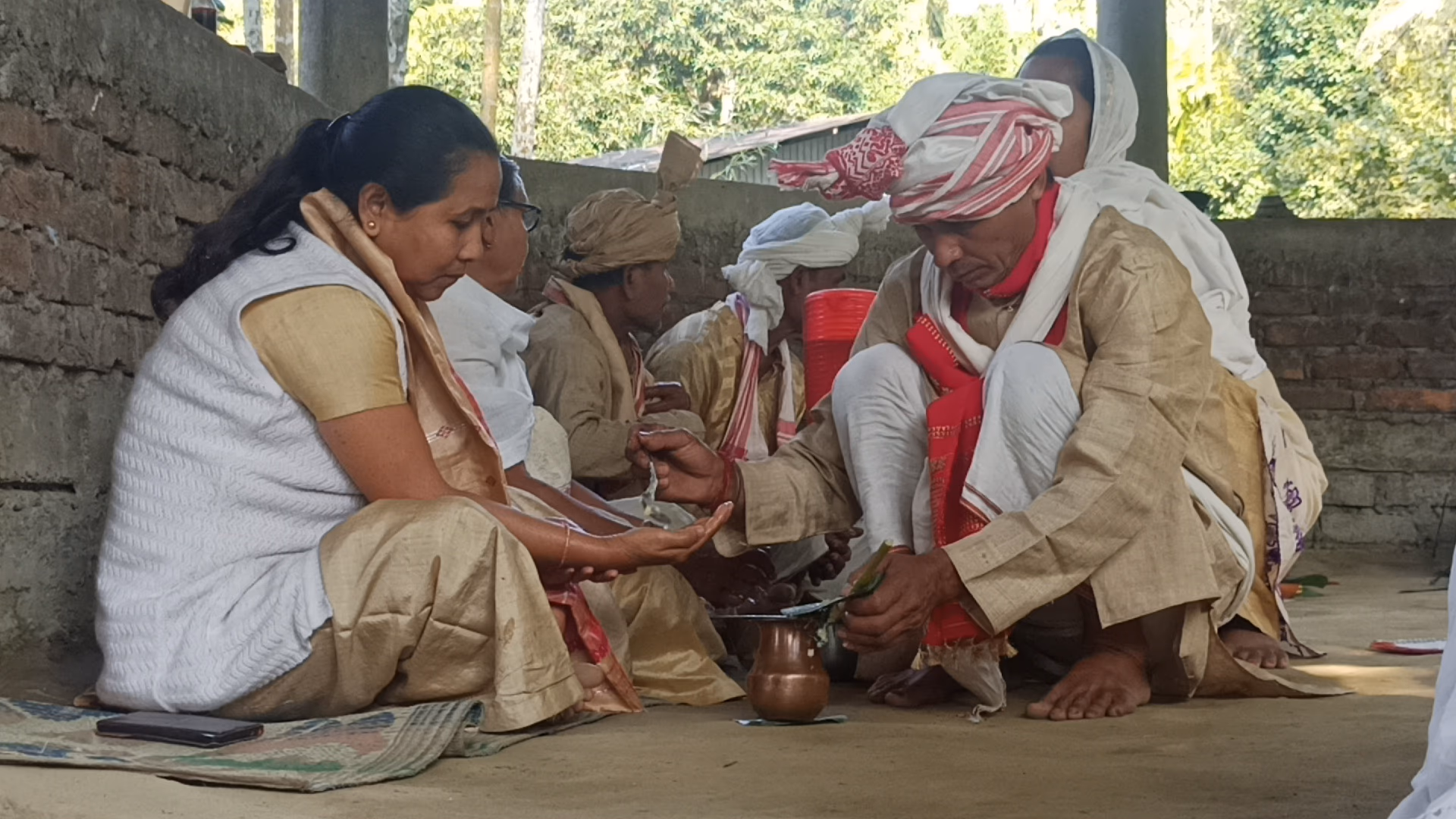 Men and women in traditional Tai-Ahom dress seated on the ground making an offering during Me-Dam-Me-Phi