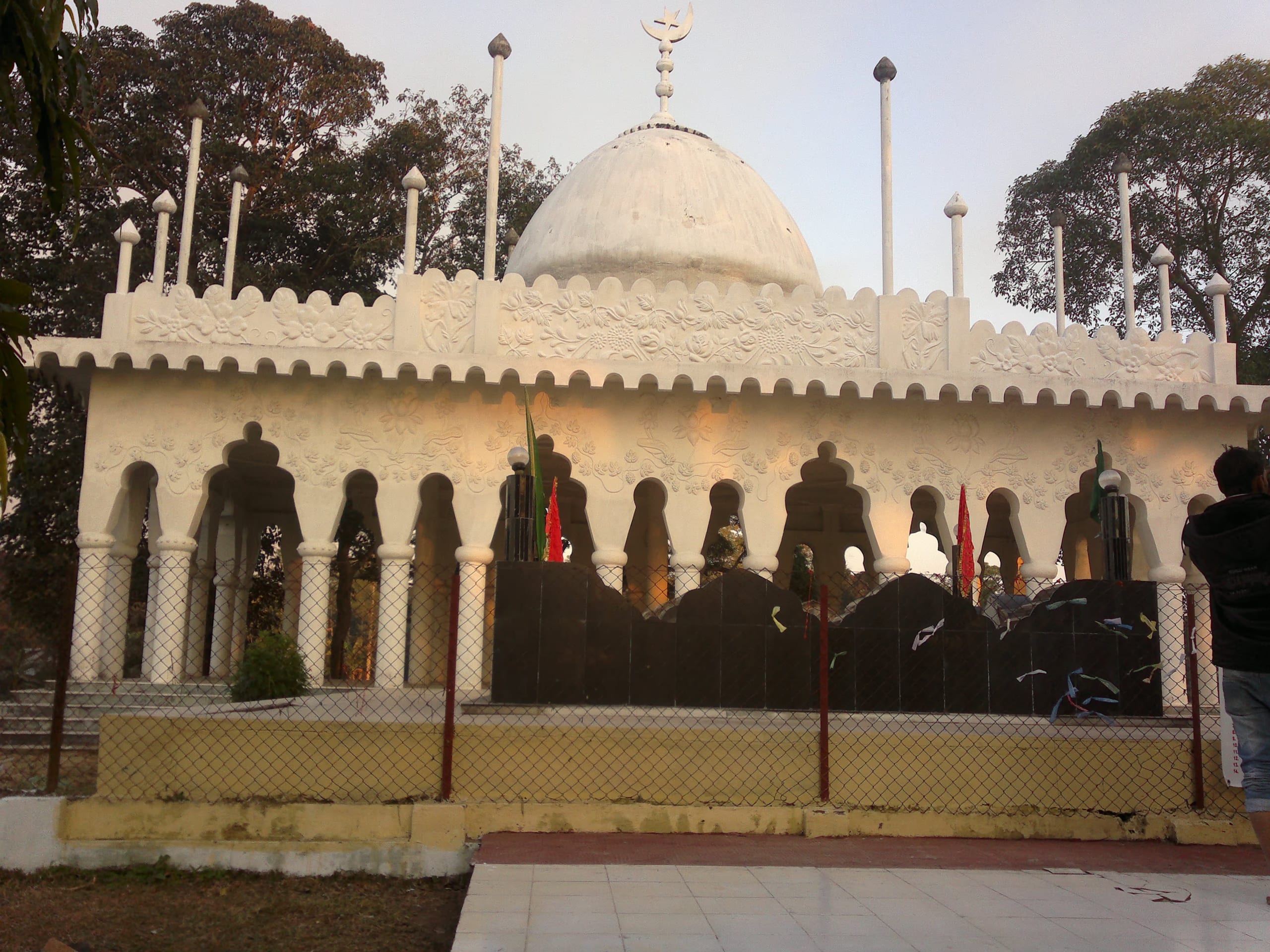 Whitewashed domed Sufi shrine with scalloped parapet, floral relief and an arched colonnade, crescent finial above the dome